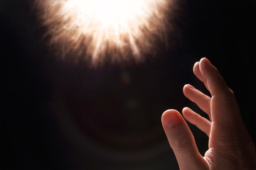 A male human hand reaches out towards a circle of light in the darkness.