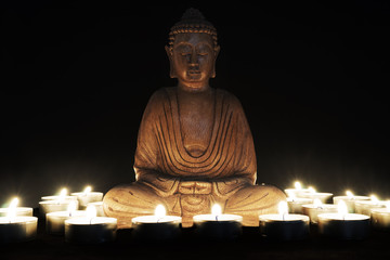 Fototapeta premium Wooden statue of Buddha with candles around him