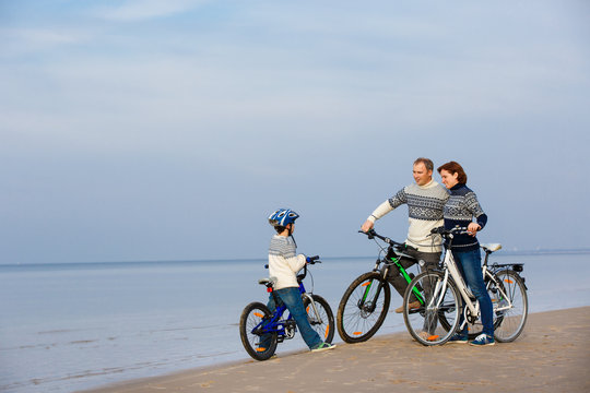 Young family of three riding bicycles on beach