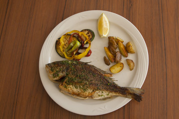 Dorada with potatoes, lemon and paper on the plate