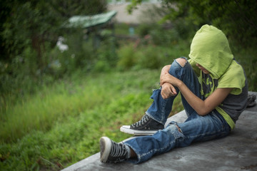 a homeless boy sits on a bench with her head bowed down