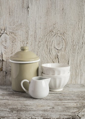 Vintage crockery - enamel jug and white ceramic bowl on bright wooden surface. Rustic style