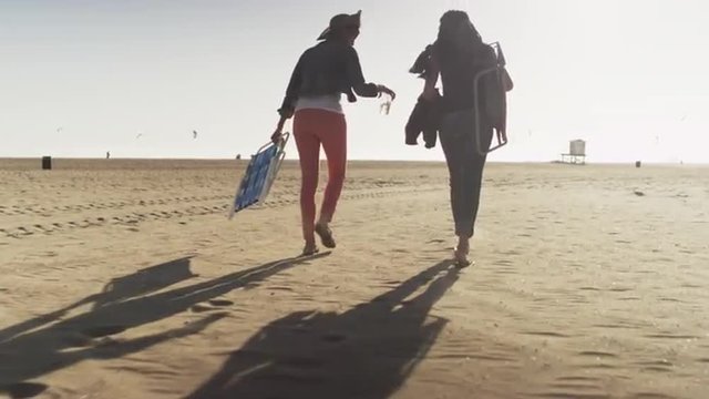 Two women walking out towards the ocean across a large sandy beach
