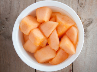 closeup melon slice in white dish with wood table background