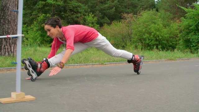 Slow motion shot of an inline skater performing front splits to skate under a limbo bar 