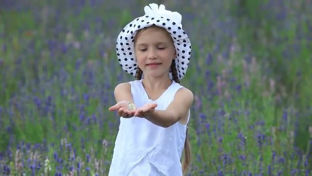 Girl holding a butterfly. Girl in white hat standing in a field and smiling at camera