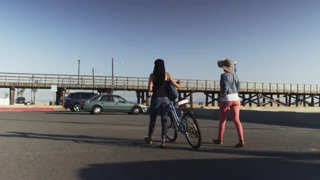 Two Black Women Friends Walking Bike Through Parking Lot At The Beach On Sunny Day