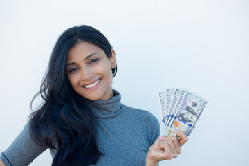 Closeup portrait, excited successful young business woman in gray shirt holding money dollar bills in hand, isolated white wall background. Positive emotion facial expression feeling. Financial reward