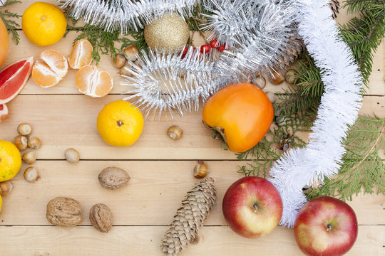Tangerines in Christmas decor with Christmas tree, nuts and apples on light wooden background