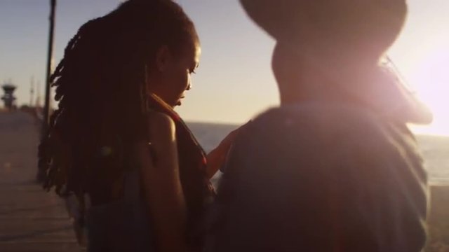 Black women best friends sharing mobilel phone pictures on pier at sunset