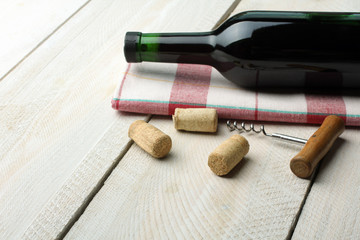 a bottle of wine on a napkin and corkscrew with cork on white wooden background