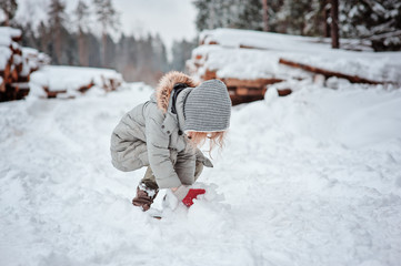 child girl playing with snow in winter walk in forest, outdoor activities