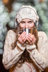 Young woman with headphones and hot tea outdoors winter portrait