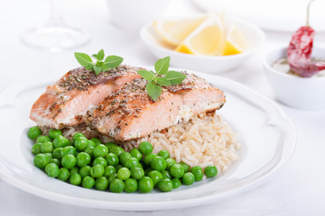 Baked salmon with rice, green peas and basil on a white ceramic plate on a white background