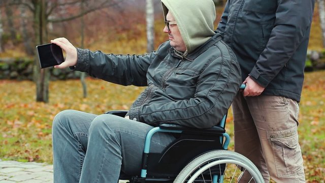 Disabled man filmed with smartphone in wheelchair with assistant behind