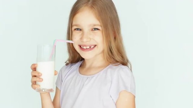 Happy child drinking milk. Girl with beautiful blond hair on a white background. Thumb up. Ok. Closeup