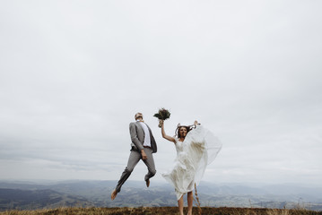 Obraz premium beautiful fabulous happy bride and stylish groom jumping on th