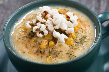 corn soup with popcorn in cup on wooden table, closeup