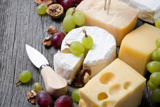 different cheeses, grapes and walnuts on a wooden background