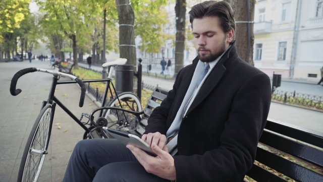 businessman using a tablet sitting on a bench near the bicycle 