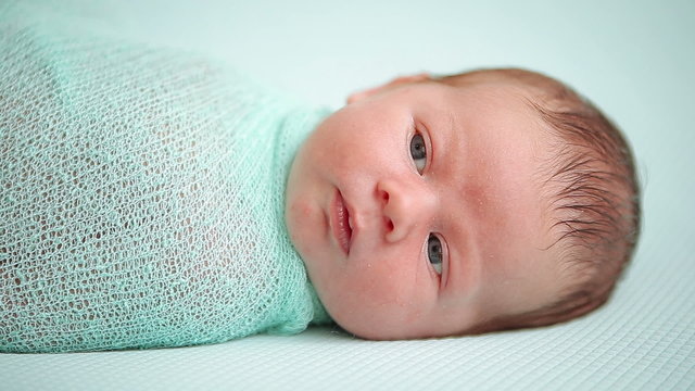 Blue-eyed newborn baby lying and looking around in wonder