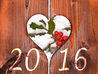 2016, wooden frame in the shape of a heart and branch of holly under the snow in the background