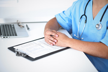 Fototapeta premium Portrait of unknown male surgeon doctor sitting at the table in hospital office, stethoscope