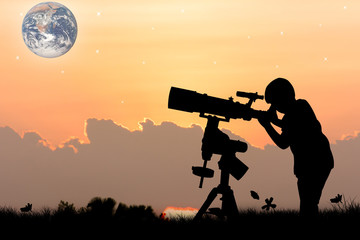 Fototapeta na wymiar silhouette of little boy looking through a telescope at sunset background,the backdrop of the planet earth. Elements of this image furnished by NASA.