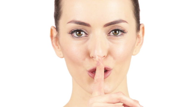 Attractive young woman smiling and holding a finger to her lips expressing silence