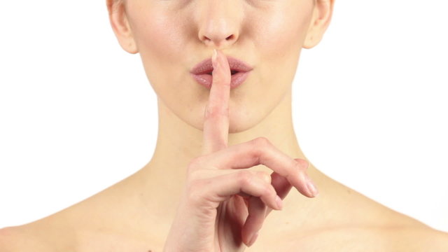 Attractive young woman smiling and holding a finger to her lips expressing silence