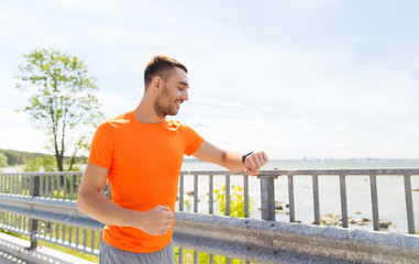 smiling young man with smart wristwatch at seaside