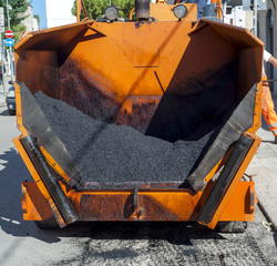 Tracked paver laying fresh asphalt during road repairing