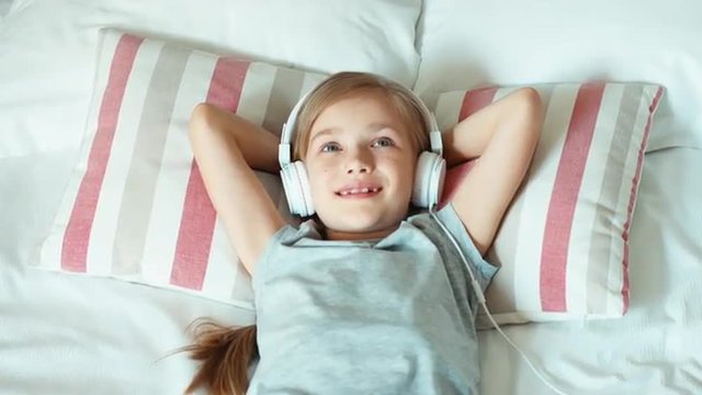 Portrait girl child listening music in headphones and lying on the bed. Zooming
