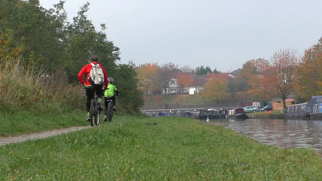 Family, father and son on bicycles passing narrow boats moored at Bridgewater canal marina in autumn on a misty day