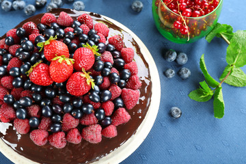 Delicious chocolate cake with summer berries on blue tablecloth, closeup