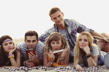 Joyful friends with musical instruments lying on the sand near the river