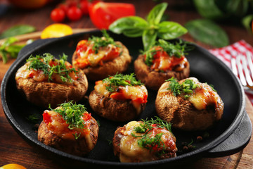 A frying pan with stuffed mushrooms and vegetables on the table