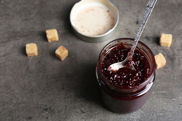 A jar of tasty jam, a spoon and crackers on grey background