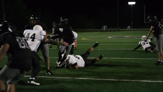 A football player fights his way down the field toward the end zone at night