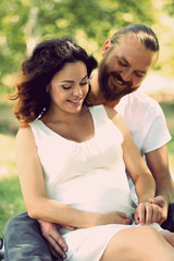 Lovely smiling couple embrace sitting on white blanket in the park, close up