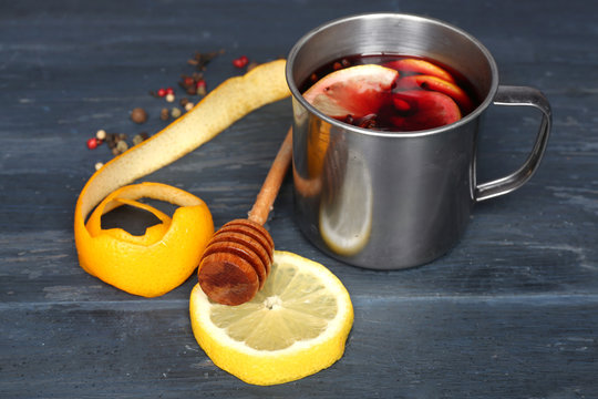 Mulled wine in a mug with citruses on grey wooden background, close up