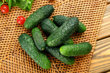 Composition of cucumbers, tomatoes and sweet peppers on wicker serviette against wooden background, close up