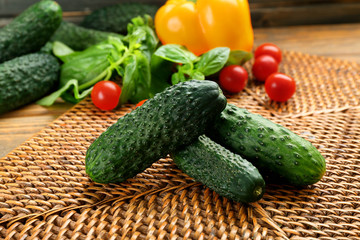 Composition of cucumbers, tomatoes and sweet peppers on wicker serviette against wooden background