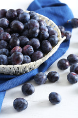 Fresh plums in basket on the white wooden background