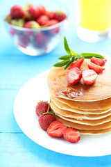 Tasty pancakes with strawberry on blue wooden background