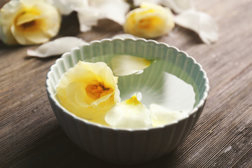 Flower petals in bowl with water on wooden background