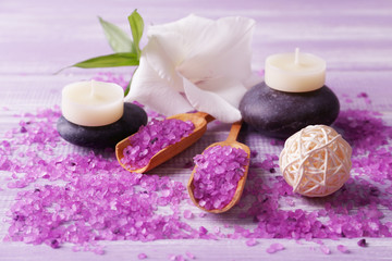 Spa composition of candles, stones, sea salt and flower on purple wooden background
