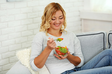 Beautiful woman with salad on home interior background