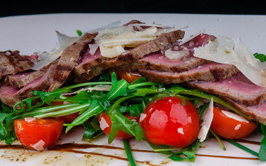 Medium rare steak served on a plate with cherry tomatoes and arugula. On top of it is grated parmesan cheese.