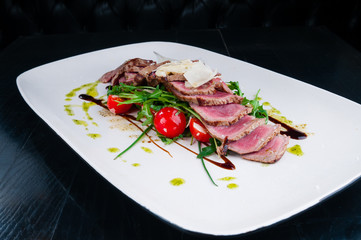 Medium rare steak served on a plate with cherry tomatoes and arugula. On top of it is grated parmesan cheese.